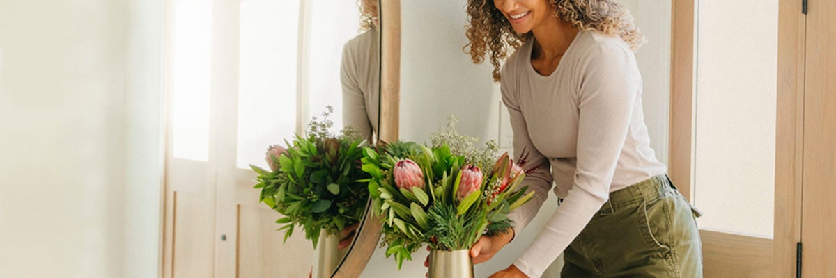 Woman arranging a vibrant floral bouquet with lush greenery in a stylish interior setting.