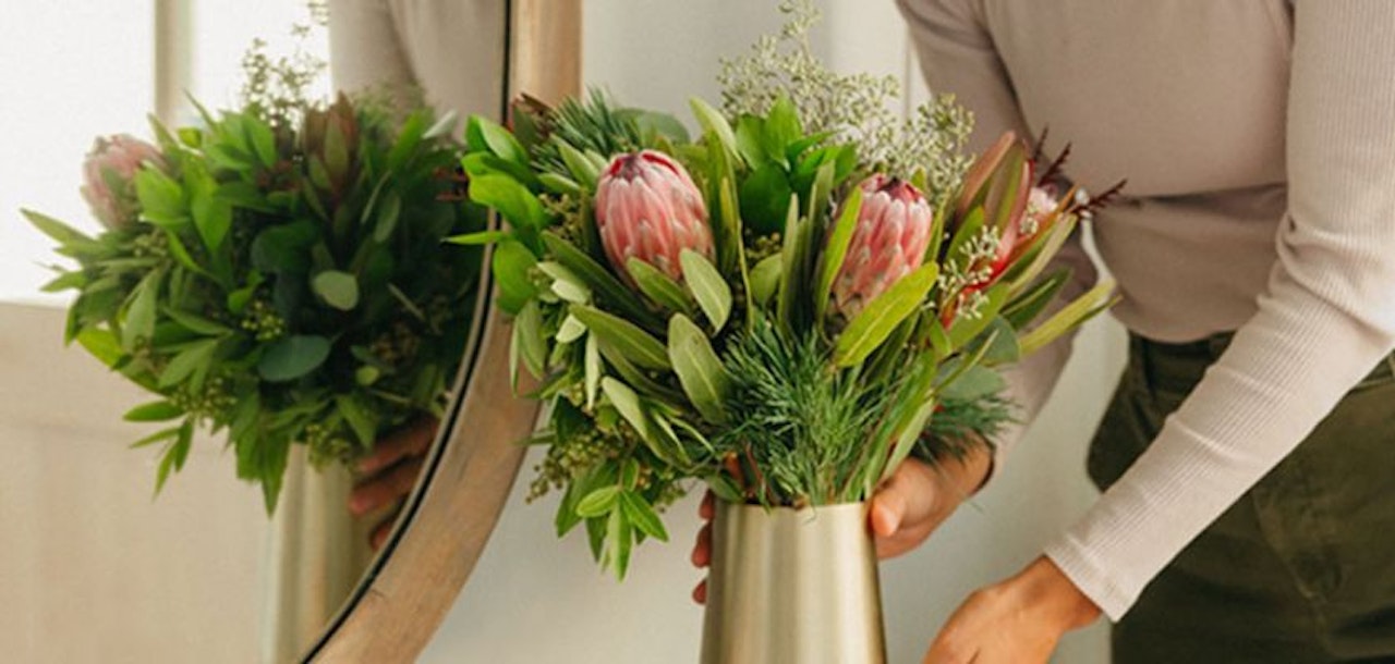 A stylish floral arrangement featuring vibrant greenery and striking protea blossoms in a modern vase.