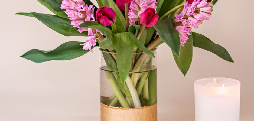 Vibrant arrangement of pink tulips and hyacinths in a stylish glass vase beside a soft white candle.