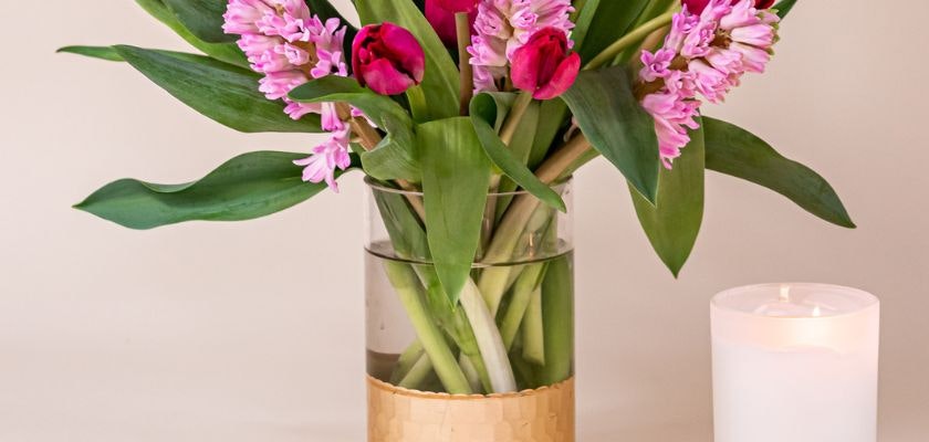 Vibrant arrangement of pink tulips and hyacinths in a stylish glass vase beside a soft white candle.