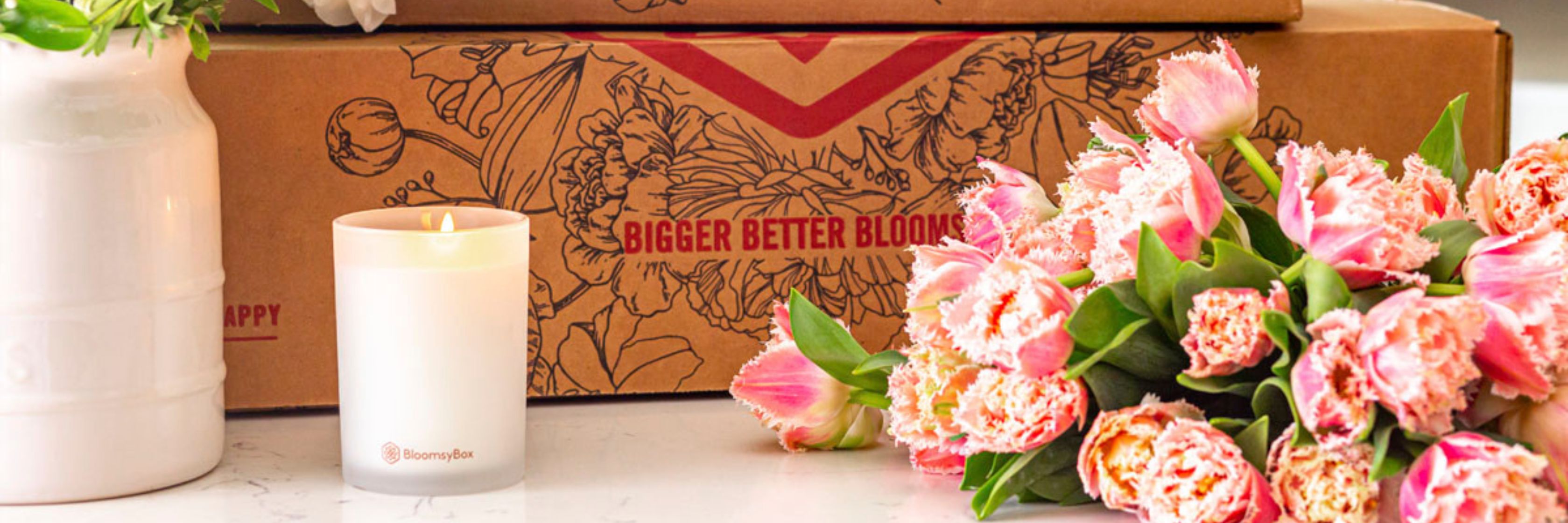 Elegant pink tulips next to a candle and a subscription box, perfect for floral delivery lovers.