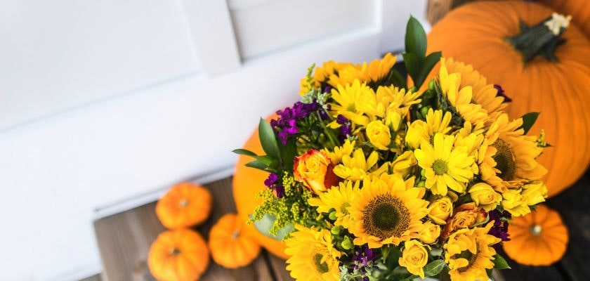 Vibrant fall floral arrangement featuring sunflowers and colorful blooms beside pumpkins.