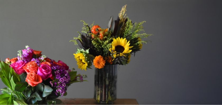 Vibrant floral arrangement featuring sunflowers, orange blooms, and lush greenery in a modern vase.