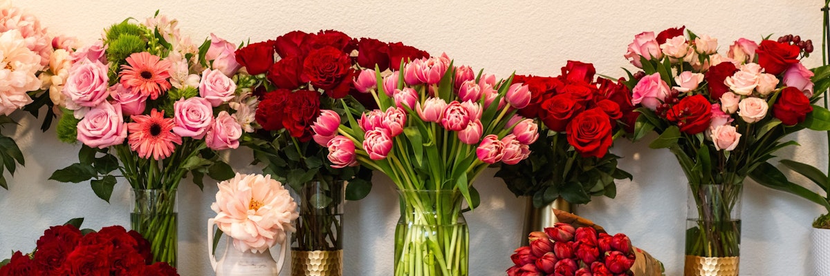 Vibrant floral display featuring red and pink roses, tulips, and gerbera daisies in elegant vases.
