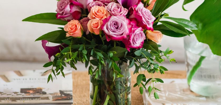 Vibrant floral arrangement featuring pink and orange roses with lush greenery in a glass vase.