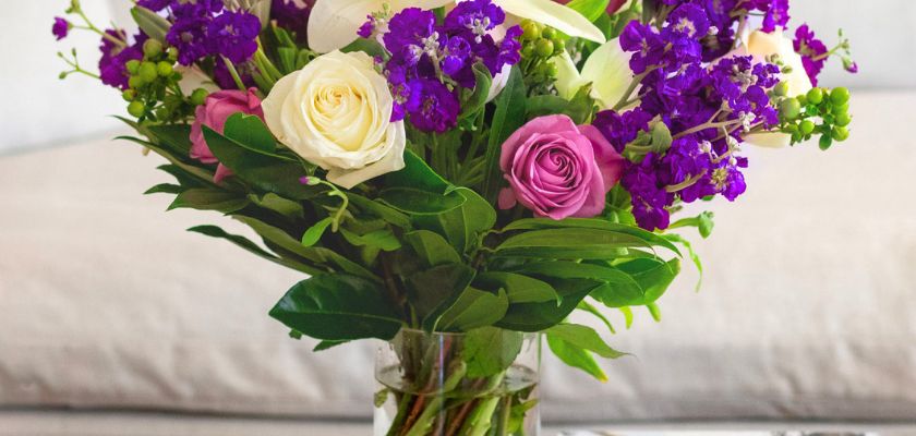 Vibrant floral bouquet featuring white roses, purple blooms, and fresh greenery in a glass vase.