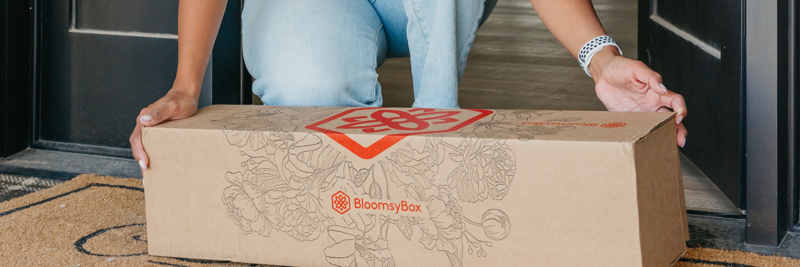Person receiving a BloomsyBox delivery with a beautiful flower arrangement at home.