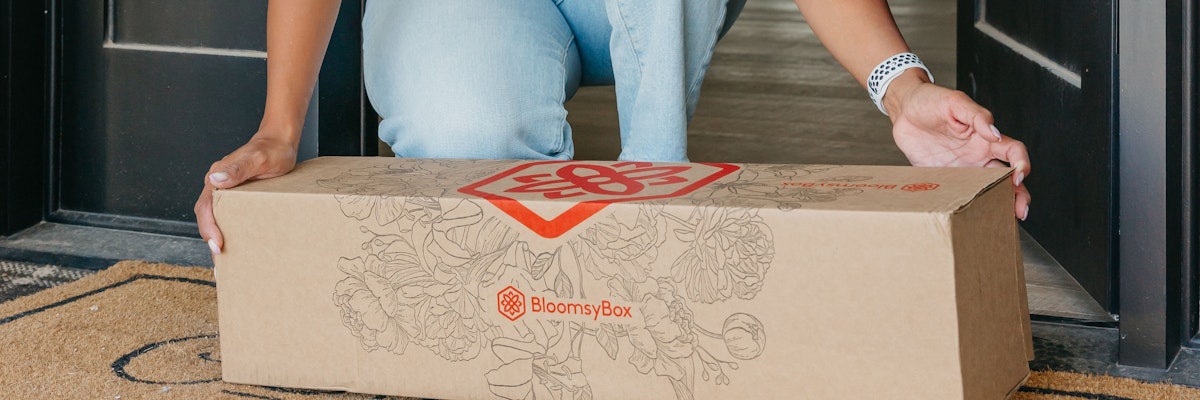 Person receiving a BloomsyBox delivery with a beautiful flower arrangement at home.