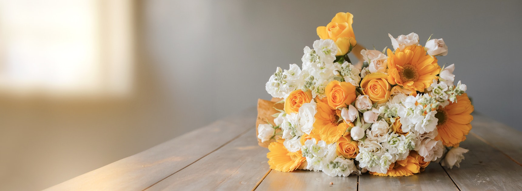Bright floral arrangement featuring yellow roses and gerbera daisies on a rustic table.