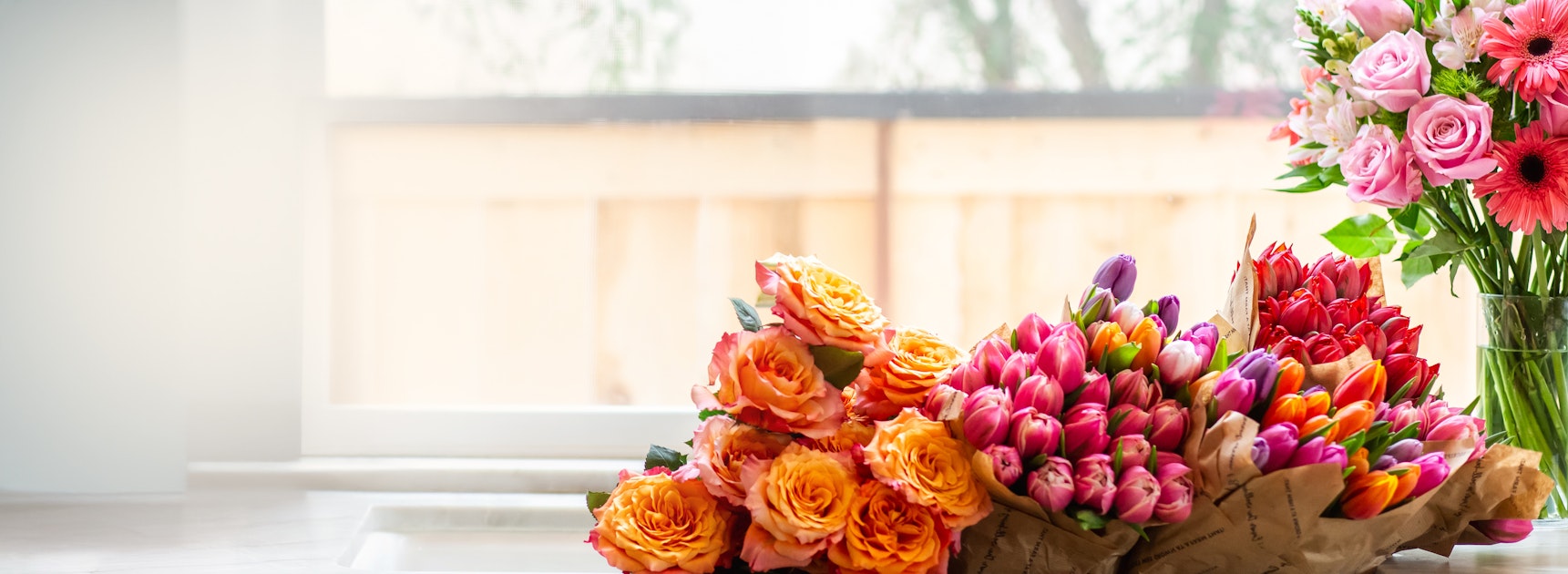 Vibrant floral display featuring pink roses and colorful tulips beside a sunny window.