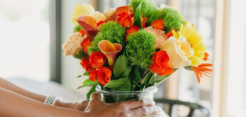 Vibrant floral arrangement featuring orange roses, yellow blooms, and lush greenery in a vase.