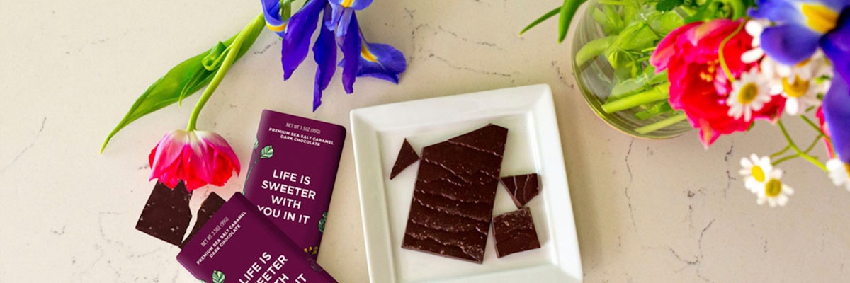 Delicious dark chocolate pieces on a plate beside vibrant flowers and cheerful gift cards.