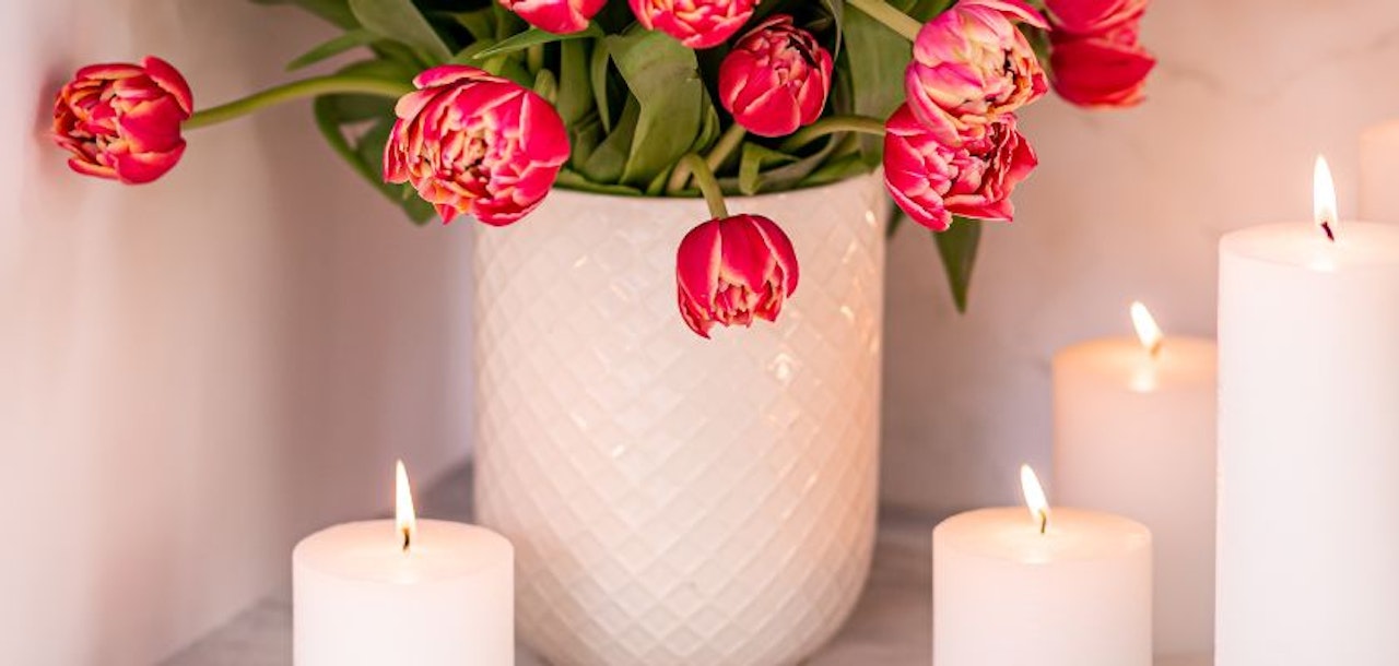 Elegant pink tulips in a textured white vase surrounded by lit candles, creating a serene ambiance.