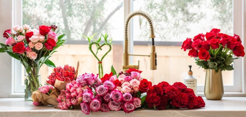 Vibrant display of assorted roses and flowers arranged by a kitchen sink, showcasing floral beauty.