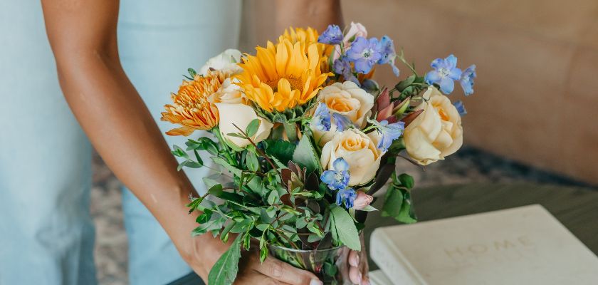 A vibrant bouquet featuring sunflowers, roses, and blue delphiniums for a cheerful ambiance.