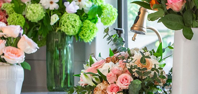A charming floral arrangement featuring pink roses and lush greenery in a bright kitchen setting.