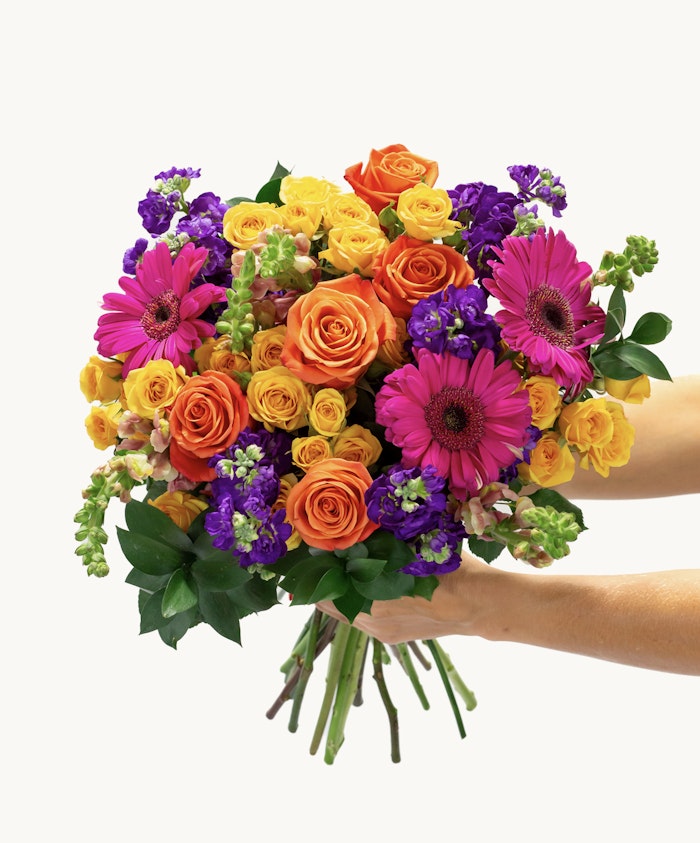 Bright and cheerful bouquet featuring orange roses, pink gerbera daisies, and vibrant green foliage.