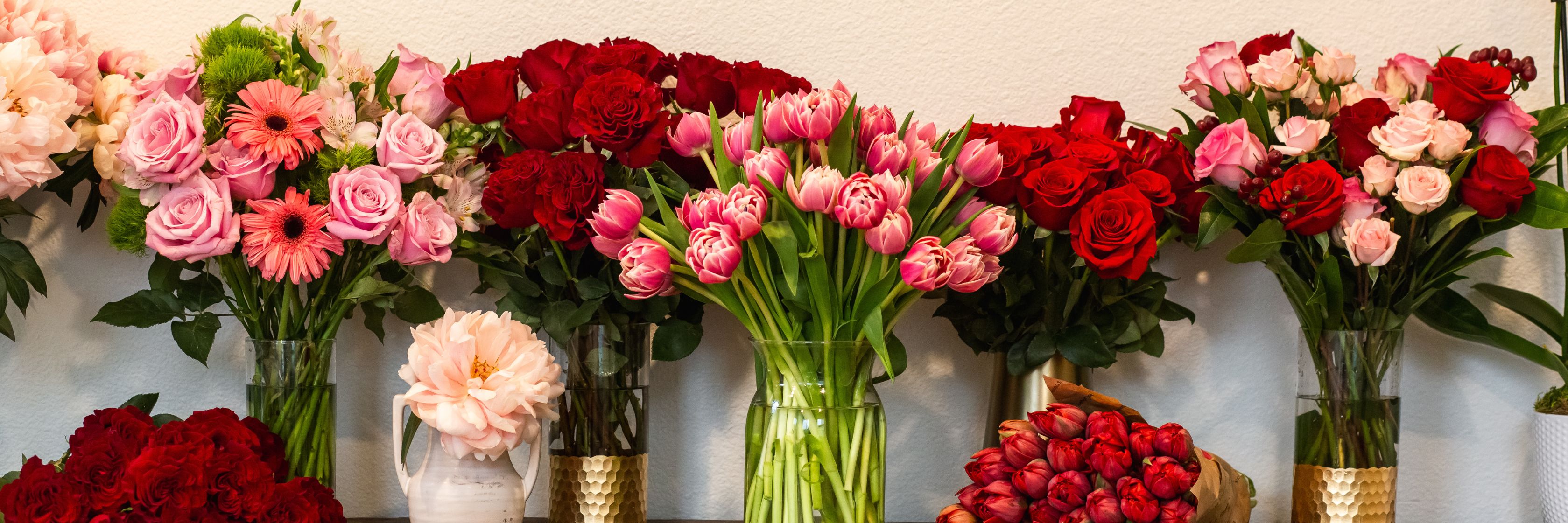 Vibrant floral display featuring red and pink roses, tulips, and gerbera daisies in elegant vases.