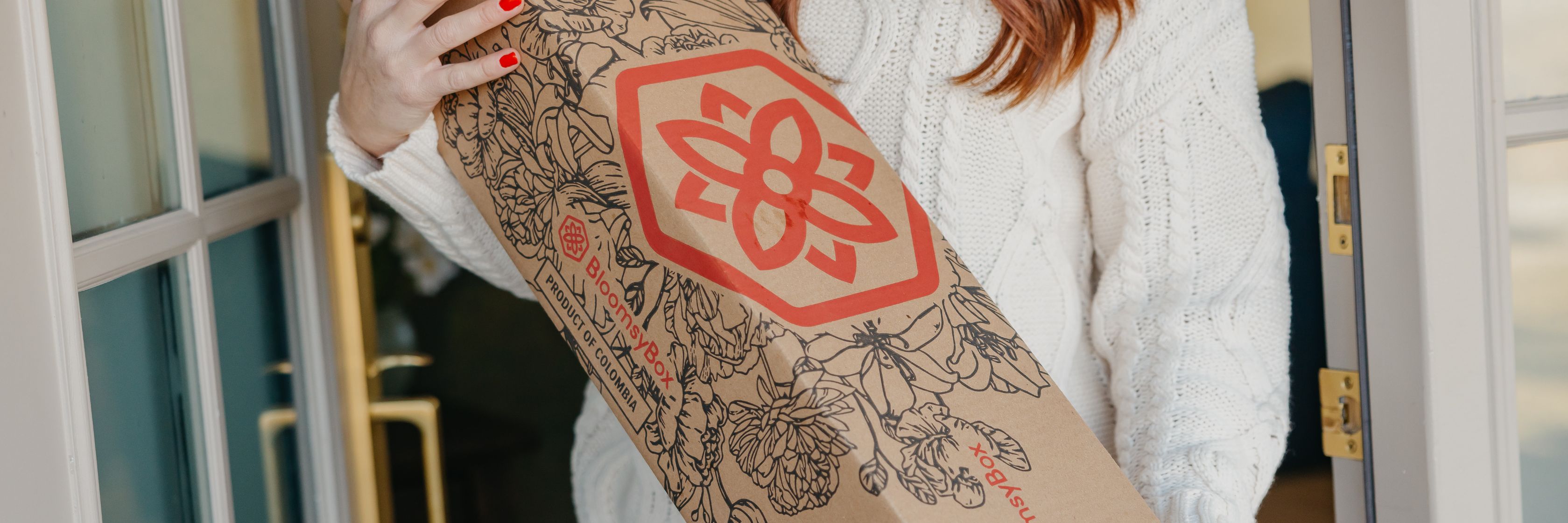 A woman wearing a cozy sweater holds a stylish floral delivery box, showcasing intricate designs.