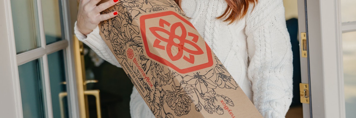 A woman wearing a cozy sweater holds a stylish floral delivery box, showcasing intricate designs.