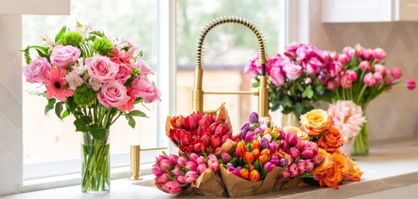 Vibrant floral arrangement featuring pink roses, tulips, and spring blooms in a sunlit kitchen.