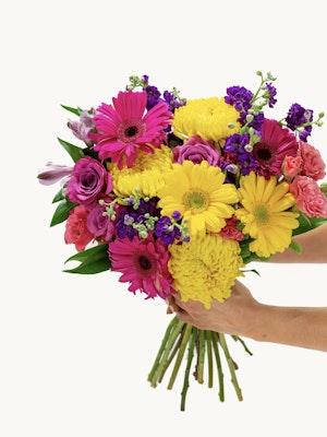 Vibrant bouquet featuring pink gerbera daisies, yellow chrysanthemums, and purple blooms.