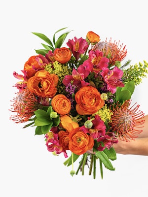 Vibrant bouquet featuring orange ranunculus, protea, and pink alstroemeria blooms.