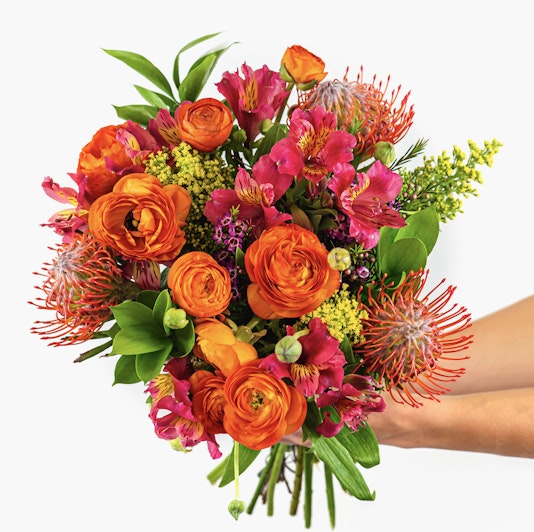 Vibrant bouquet featuring orange ranunculus, protea, and pink alstroemeria blooms.