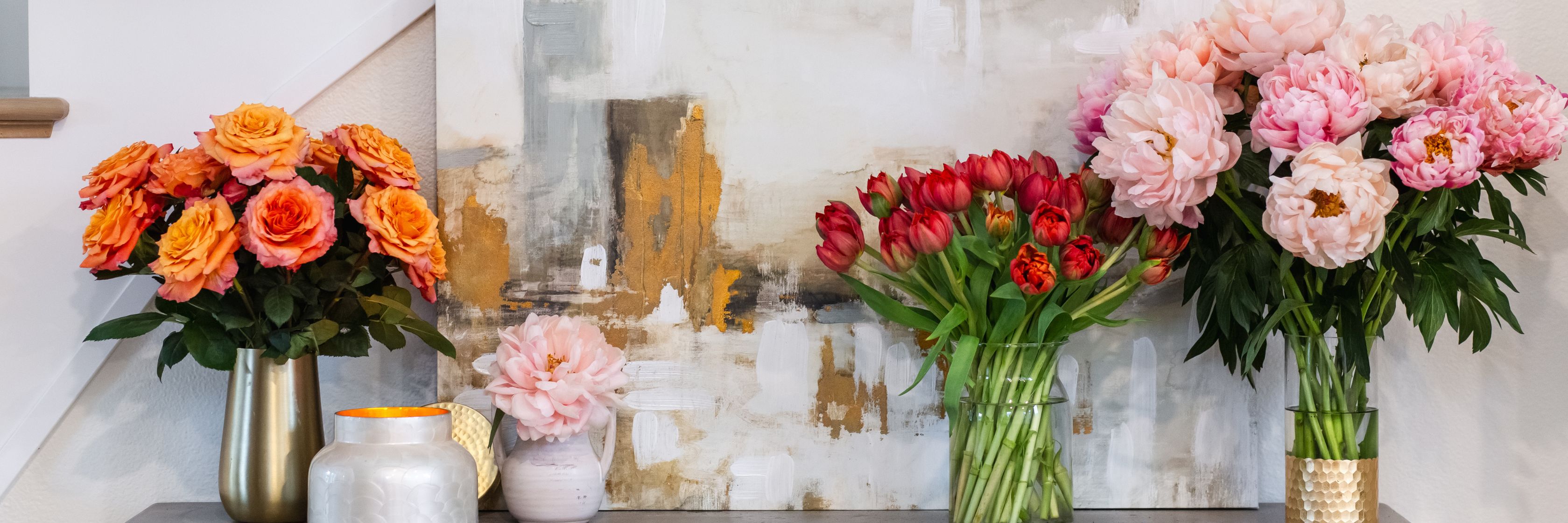 Vibrant floral display with pink peonies and orange roses beside a contemporary art piece.