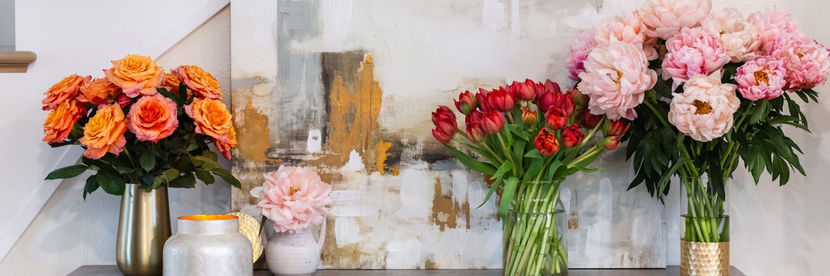 Vibrant floral display with pink peonies and orange roses beside a contemporary art piece.