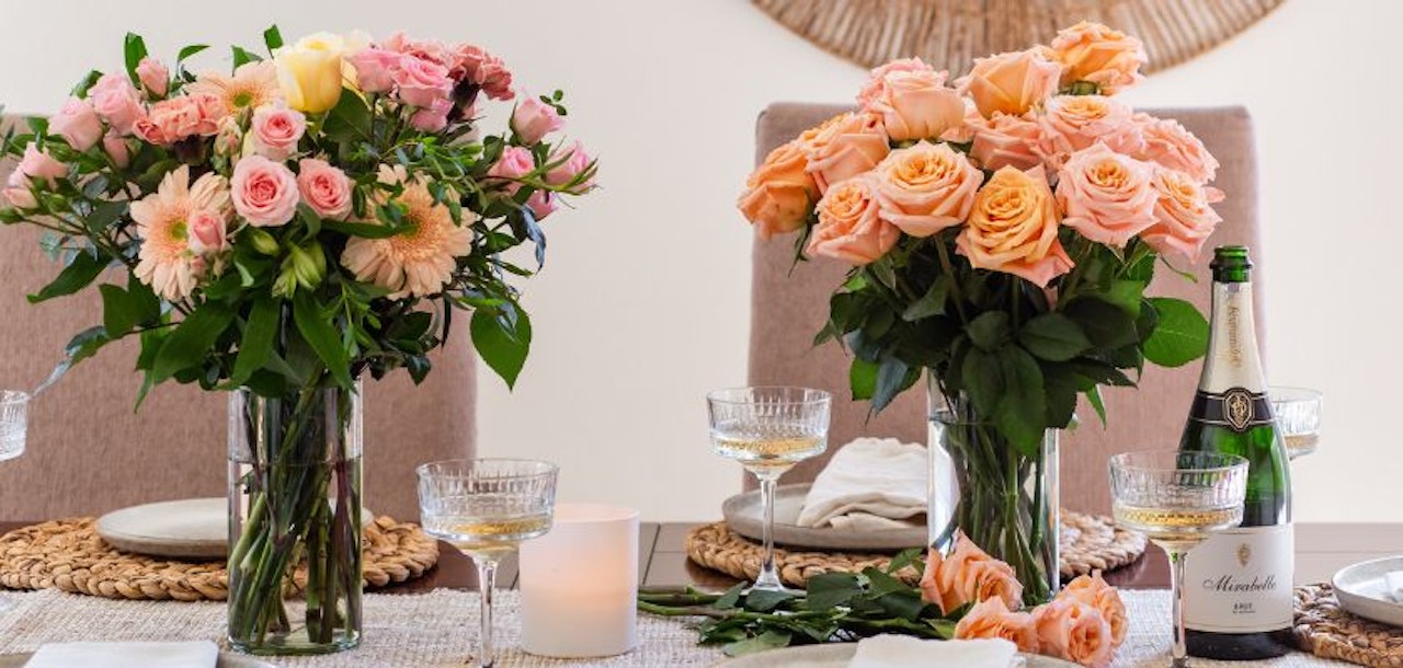 Elegant floral arrangements of peach and pink roses on a dining table, complemented by sparkling wine.