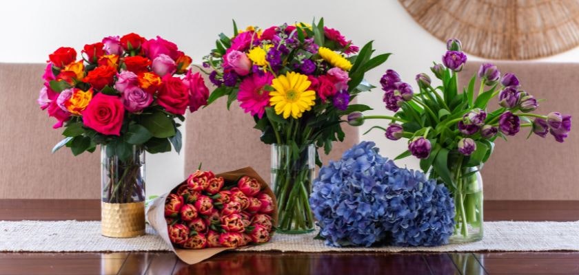Vibrant flower arrangements featuring roses, tulips, and hydrangeas on a dining table.