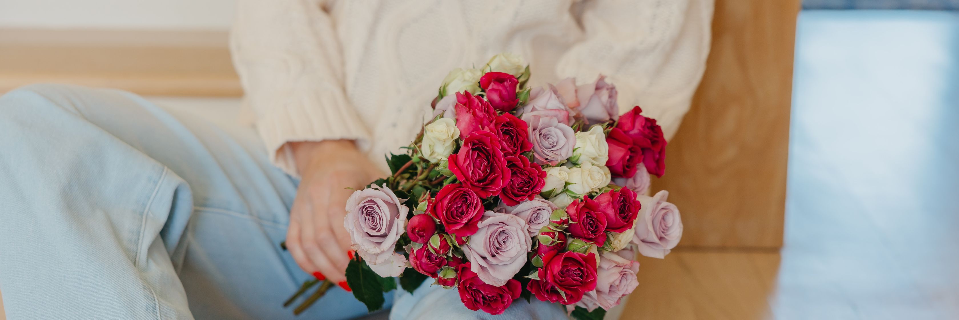 A vibrant bouquet featuring pink and red roses held by a person in cozy attire, perfect for gifting.