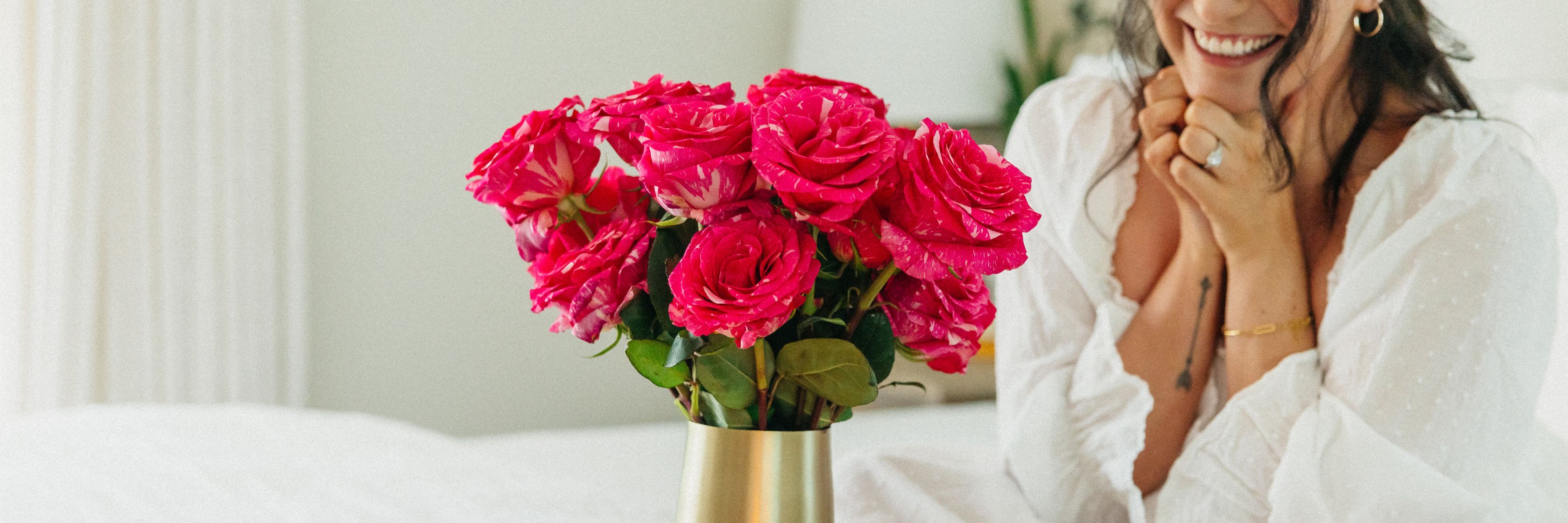 Vibrant pink roses in a gold vase, enhancing a cozy bedroom setting with natural beauty.
