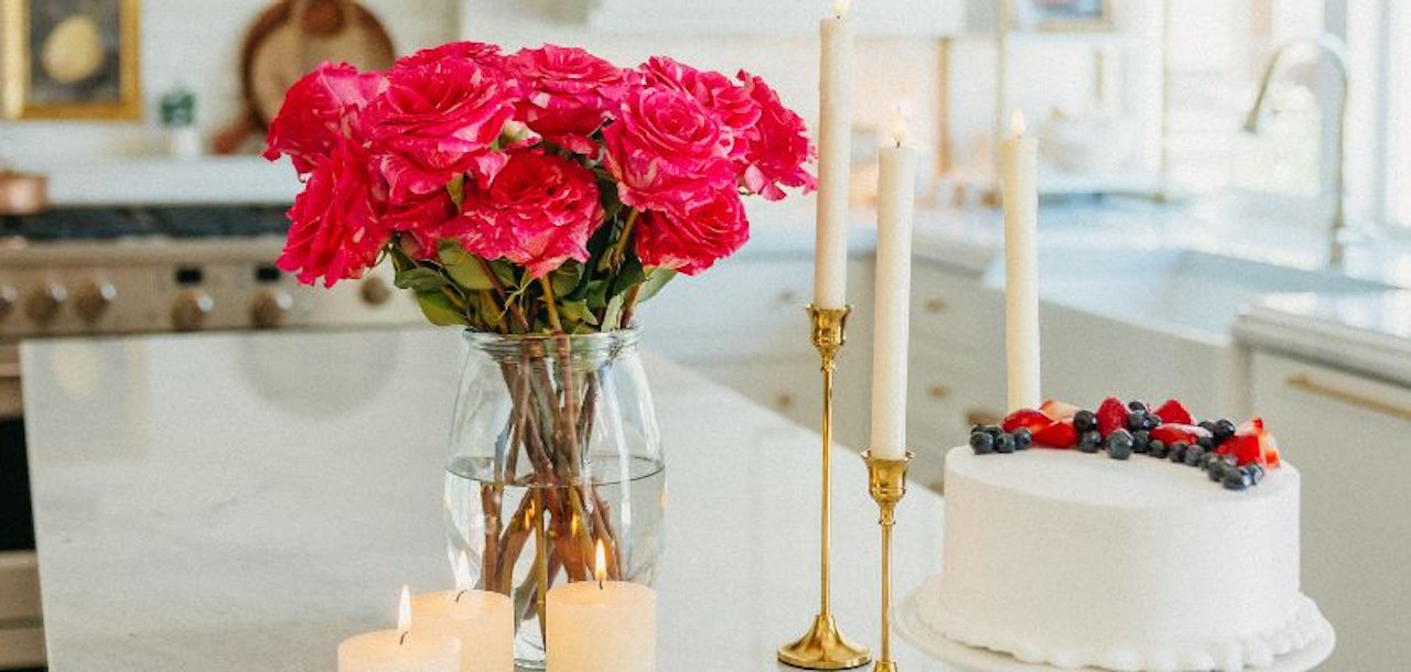 Vibrant pink roses in a glass vase beside a white cake and candles, creating a festive birthday atmosphere.