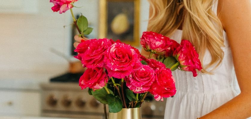 A vibrant bouquet of pink roses held by a woman in a cozy kitchen, adding charm to the space.