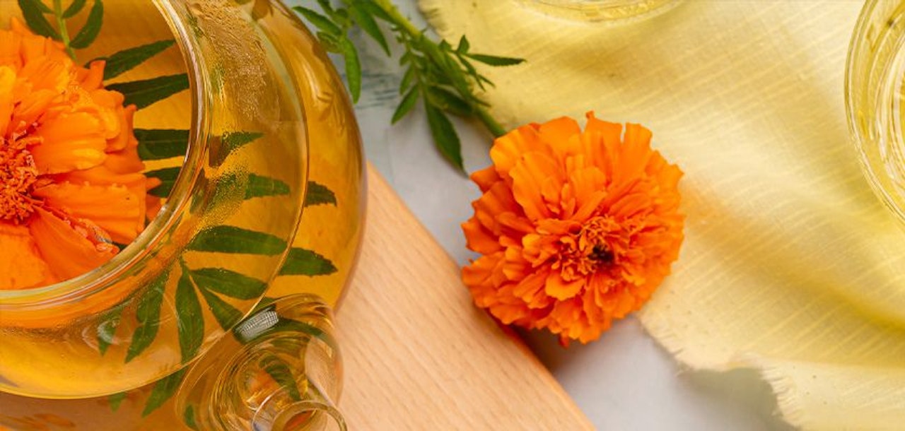 Vibrant orange marigold tea with fresh leaves, beautifully arranged for a refreshing herbal experience.