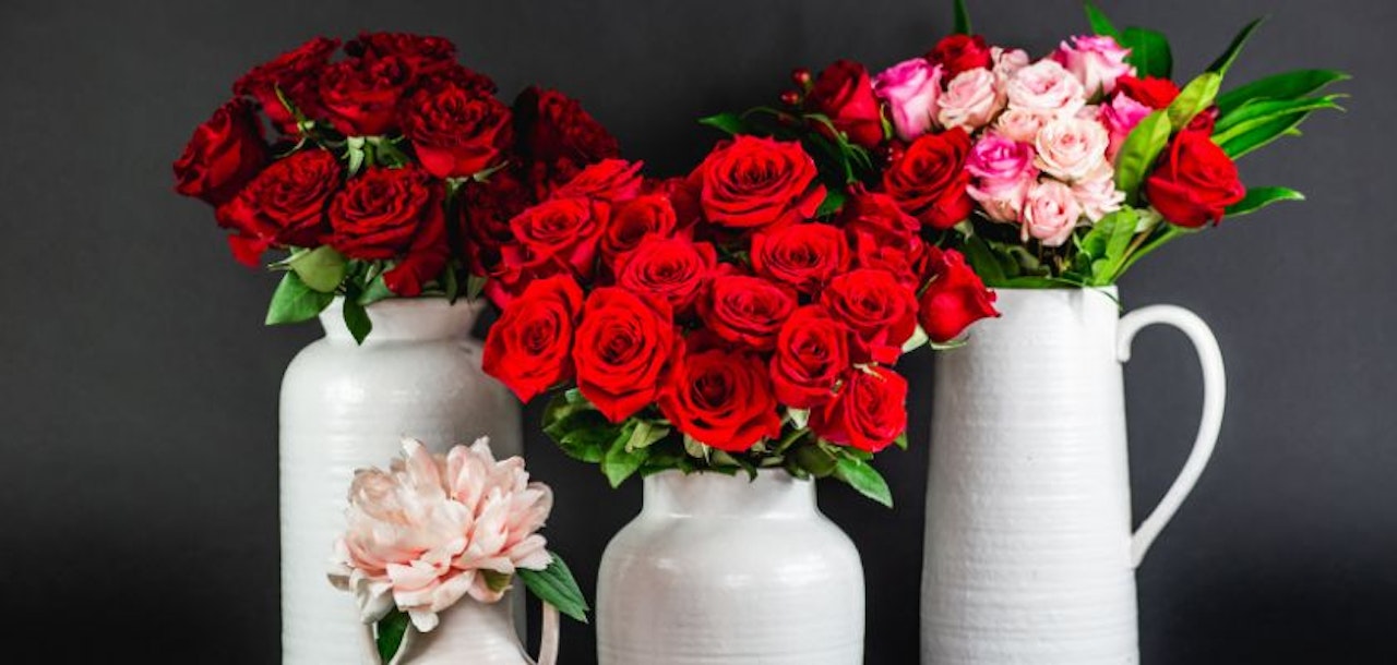 Elegant floral arrangement featuring vibrant red roses and soft pink blooms in white pitchers.