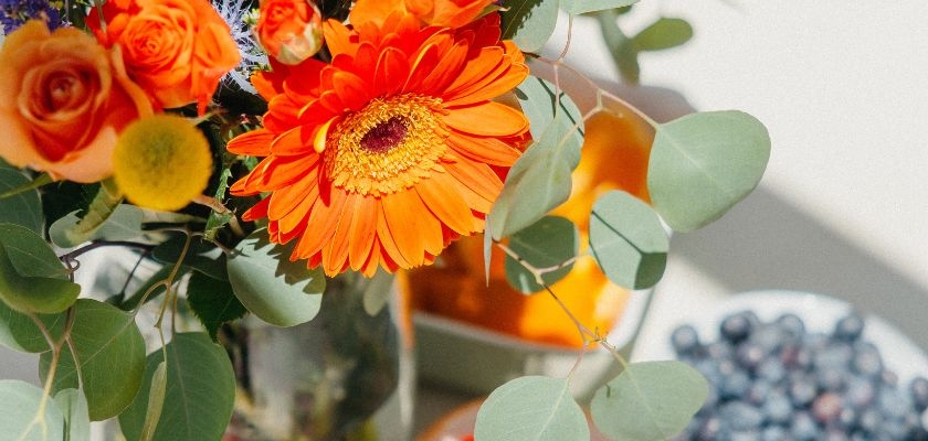 Bright orange gerbera daisies and roses arranged with lush greenery in a vibrant bouquet.
