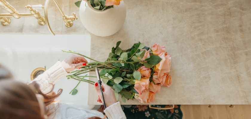 A person carefully trimming peach roses on a marble countertop before arranging them.
