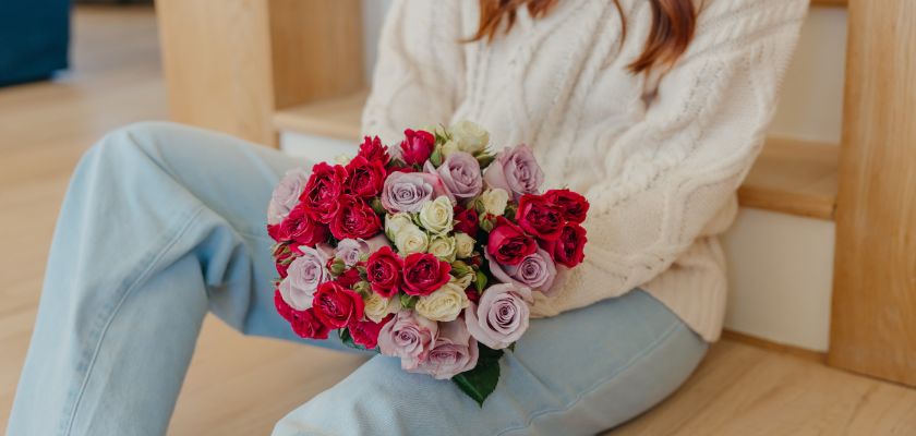 A beautiful bouquet of red and lavender roses held by a woman in a cozy sweater.