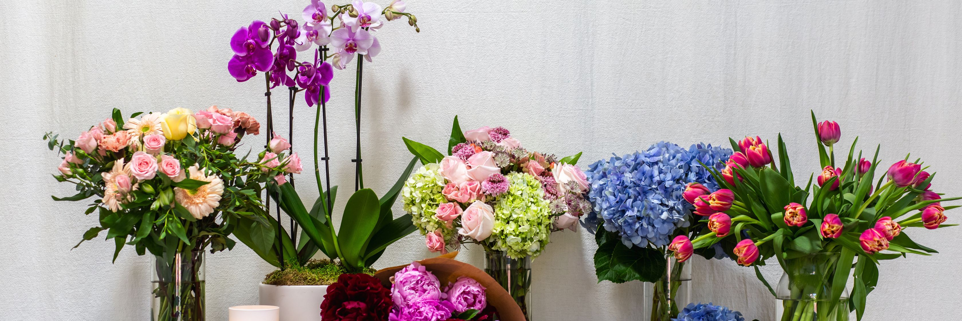 Colorful floral arrangement featuring roses, tulips, and orchids in elegant vases.