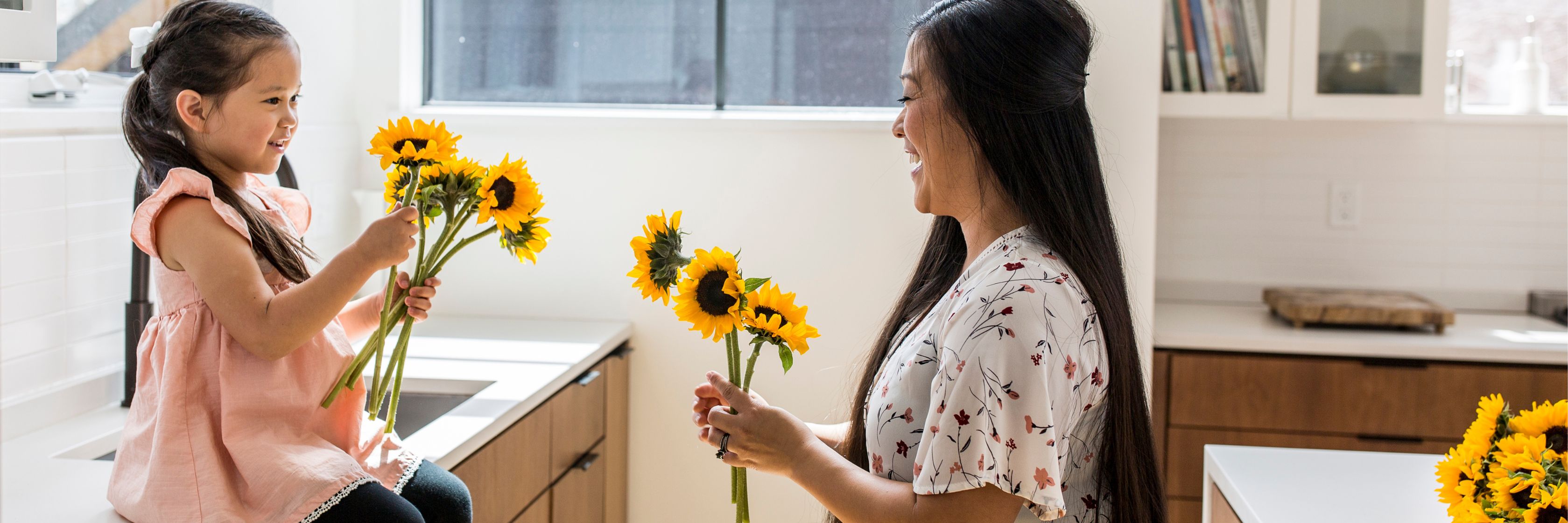 A joyful moment between a mother and daughter sharing bright sunflowers in a cozy kitchen.