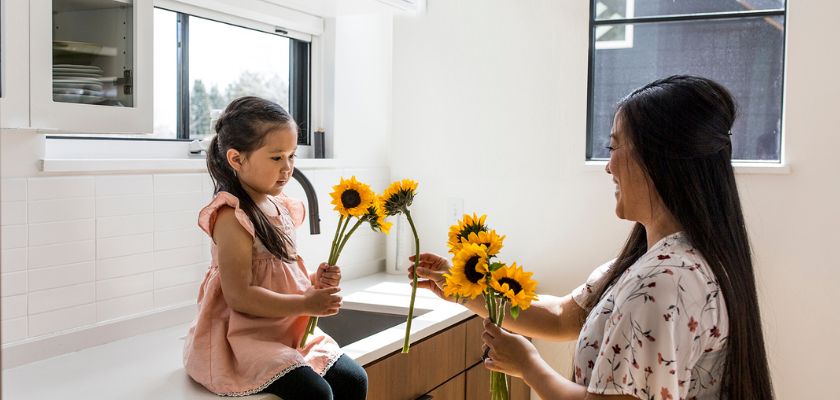 A joyful moment between a mother and daughter sharing sunflowers in a bright kitchen.