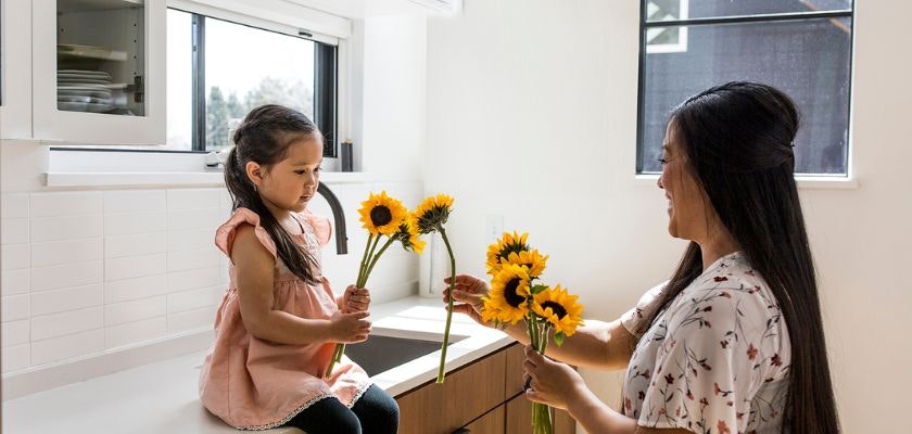 A joyful moment between a mother and daughter sharing sunflowers in a bright kitchen.