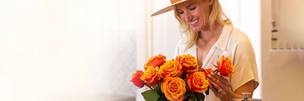 A woman arranging a vibrant bouquet of orange roses, radiating joy and warmth.