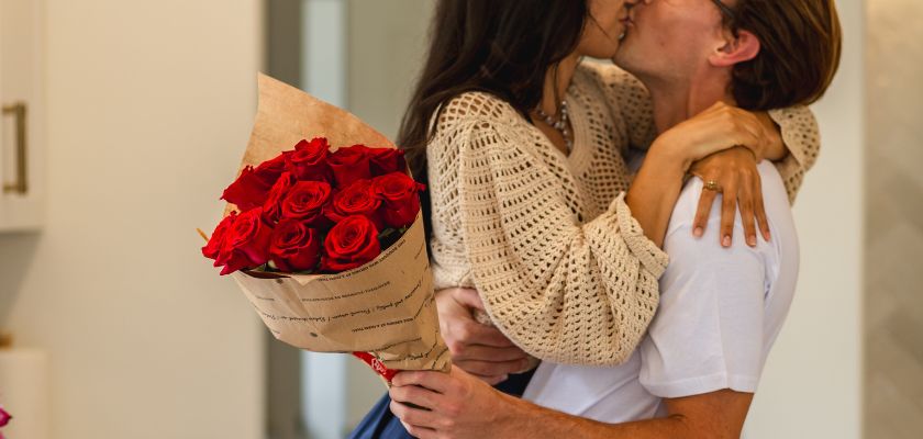A romantic couple sharing a kiss while embracing a bouquet of red roses.