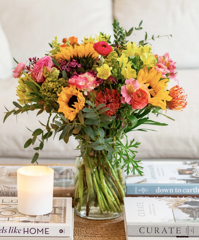 Vibrant floral arrangement featuring sunflowers, pink ranunculus, and greenery in a vase.