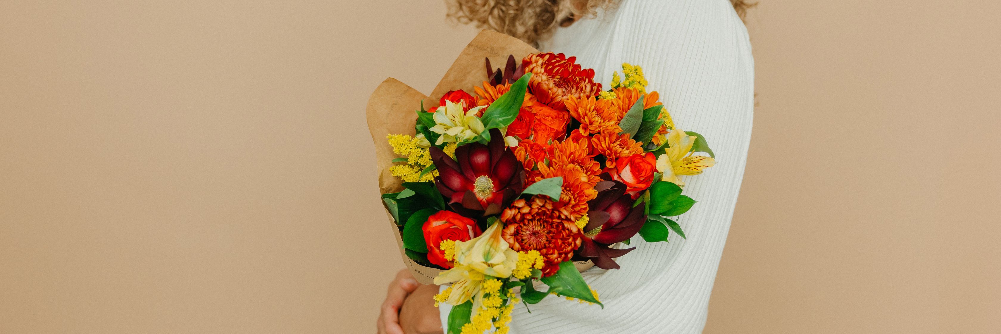 Vibrant autumn bouquet featuring orange and yellow flowers, beautifully wrapped and held.