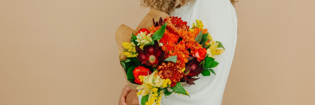 Vibrant autumn bouquet featuring orange and yellow flowers, beautifully wrapped and held.